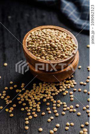Uncooked lentil legumes in bowl on black table. 109062523