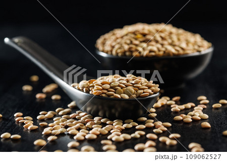 Uncooked lentil legumes in ceramic spoon on black table. 109062527
