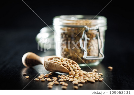 Uncooked lentil legumes in wooden scoop on black table. Uncooked lentil legumes in wooden scoop on black table. 109062531