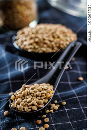 Uncooked lentil legumes in ceramic spoon on checkered napkin. Uncooked lentil legumes in ceramic spoon on checkered napkin. 109062539