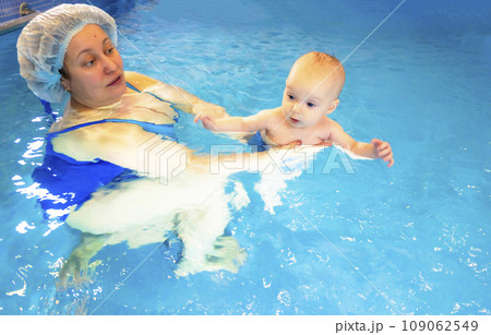 Adorable baby girl enjoying swimming in a pool with her mother early development class for infants teaching children to swim and dive.  109062549