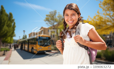 Happy Young Hispanic Girl Wearing a Backpack Near a School Bus on Campus 109063272
