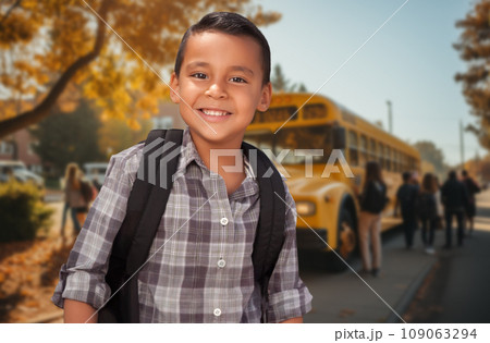 Cute Young Hispanic Boy Wearing a Backpack Near a School Bus on Campus. Cute Young Hispanic Boy Wearing a Backpack Near a School Bus on Campus. 109063294