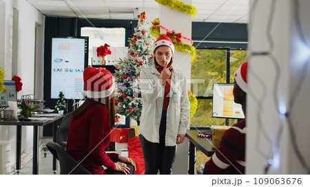 Company staff members wearing Santa Claus hat enjoying Christmas spirit mood playing pretending game during break. Coworkers having fun doing pantomime in xmas adorn office Company staff members wearing Santa Claus hat enjoying Christmas spirit mood playing pretending game during break. Coworkers having fun doing pantomime in xmas adorn office 109063676