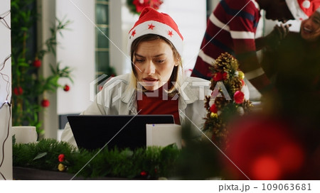 Woman filling paperwork in Christmas decorated office, perturbed by noisy coworkers discussing in background. Employee trying to concentrate on job while colleagues take shift break 109063681