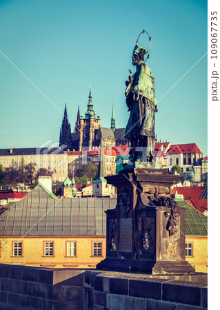 John of Nepomuk (or John Nepomucene) national saint of the Czech Republic statue on Charles Brigde at the site where the saint was thrown into Vltava with St. Vitus Cathedral in background in Prague 109067735