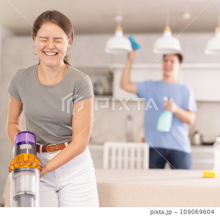 Emotional young girl laughing while vacuuming home kitchen floor 109069604