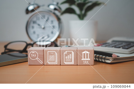 Wooden block printed tax symbols icons placed on a wooden tabletop with office supplies, financial research, reports, tax return calculations. 109069844
