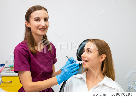 Female orthodontist examining teeth of young patient with perfect smile. 109070299