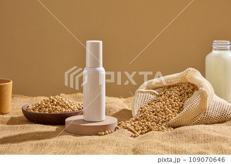 Round podium with a white bottle standing on. Mesh bag and wooden dish containing lots of soybeans displayed. Natural beauty blank label for branding mock-up concept 109070646