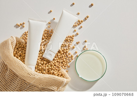 Soybean seeds and two unlabeled tubes displayed with a petri dish filled with soybean milk. White cosmetic tube for face cream, cleanser, body lotion or shampoo 109070668