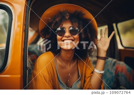 Beautiful smiling girl dressed hippie style sitting of retro travel van or car. Happy female Hispanic tourist riding along picturesque road. Summer holidays, vacation and road trip concept. Beautiful smiling girl dressed hippie style sitting of retro travel van or car. Happy female Hispanic tourist riding along picturesque road. Summer holidays, vacation and road trip concept. 109072764