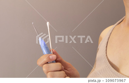 Person Holds Ear Wax Removal Glass Stick Or Curette With Led Light And Q-tip Cotton Swab In Bathroom. Personal Care Hygiene Essentials. Tool Cleaner. Horizontal Plane Person Holds Ear Wax Removal Glass Stick Or Curette With Led Light And Q-tip Cotton Swab In Bathroom. Personal Care Hygiene Essentials. Tool Cleaner. Horizontal Plane 109073967