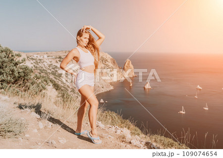 Woman summer travel sea. Happy tourist in hat enjoy taking picture outdoors for memories. Woman traveler posing on the beach at sea surrounded by volcanic mountains, sharing travel adventure journey 109074654