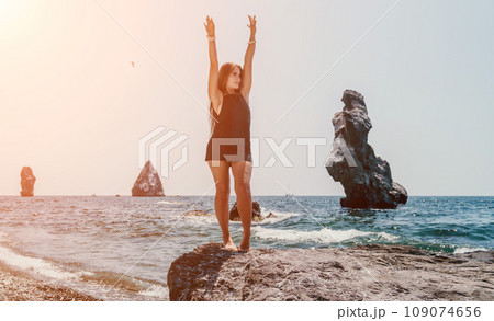 Woman summer travel sea. Happy tourist in hat enjoy taking picture outdoors for memories. Woman traveler posing on the beach at sea surrounded by volcanic mountains, sharing travel adventure journey 109074656