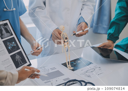Multiracial medical team having a meeting with doctors in white lab coats and surgical scrubs seated at a table discussing a patients records Multiracial medical team having a meeting with doctors in white lab coats and surgical scrubs seated at a table discussing a patients records 109074814