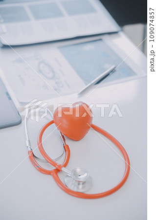 Multiracial medical team having a meeting with doctors in white lab coats and surgical scrubs seated at a table discussing a patients records 109074857