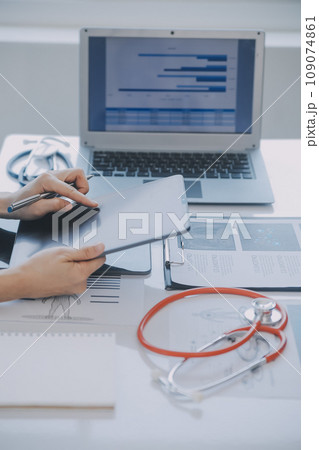 Multiracial medical team having a meeting with doctors in white lab coats and surgical scrubs seated at a table discussing a patients records Multiracial medical team having a meeting with doctors in white lab coats and surgical scrubs seated at a table discussing a patients records 109074861