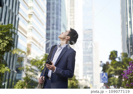 young asian business man looking up at tall buildings in downtown 109077119