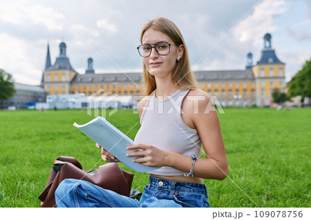 Young student girl sitting on grass, educational building background 109078756