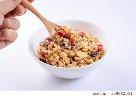 白い皿に入ったシリアルをスプーンですくう　フルーツグラノーラ　朝食　健康食品　俯瞰　白バック 109082051