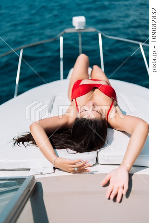 Yacht woman in a red bikini posing while on the bow of a yacht. Happy woman is sunbathing on the bow of a ship during a boat trip. Travel concept, vacation at sea 109082832