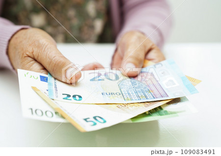 Retired elderly woman holding Euro banknotes money and worry about monthly expenses and treatment fee payment. 109083491