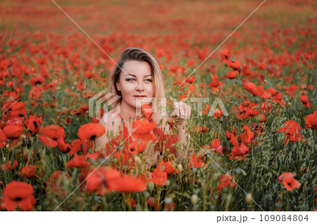 Happy woman in a red dress in a beautiful large poppy field. Blond sits in a red dress, posing on a large field of red poppies Happy woman in a red dress in a beautiful large poppy field. Blond sits in a red dress, posing on a large field of red poppies 109084804