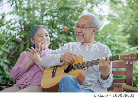 Happy Asian senior couple elderly man playing guitar while his wife singing together outdoors at home, Activity family health care, Enjoying lifestyle during retirement life having fun of senior older Happy Asian senior couple elderly man playing guitar while his wife singing together outdoors at home, Activity family health care, Enjoying lifestyle during retirement life having fun of senior older 109086032