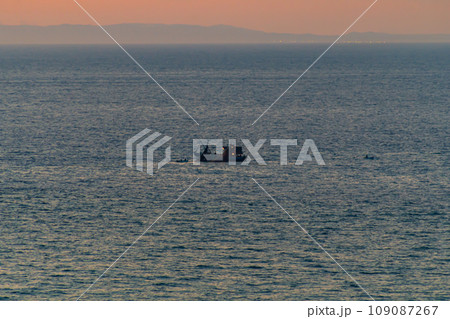 A fishing boat catches fish with nets in the ocean on the sunset horizon. Partial defocus, haze, fog. The concept of the use of natural resources, food, technology A fishing boat catches fish with nets in the ocean on the sunset horizon. Partial defocus, haze, fog. The concept of the use of natural resources, food, technology 109087267