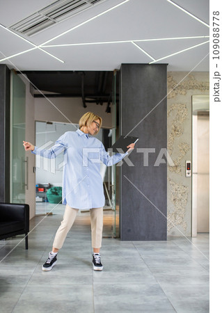 Well done woman successfully completed project, blonde businesswoman dancing outside office building in corridor at workplace. 109088778