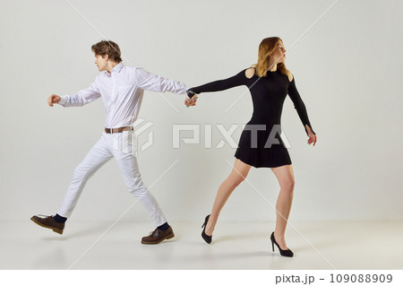 Young people trying to go in different directions, but their hands are tied with iron chains, fetters against white studio background Young people trying to go in different directions, but their hands are tied with iron chains, fetters against white studio background 109088909