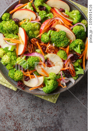 Fresh salad consisting of broccoli, apple, pecans, red onion, carrots and cranberries close-up in a plate. Vertical top view 109091416