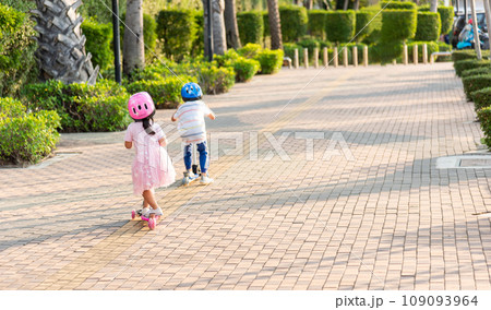 Child riding scooter. Back Asian little kid boy and girl wear safe helmet play kick board on road in park outdoors on summer day, Active children games outside, Kids sport healthy lifestyle concept Child riding scooter. Back Asian little kid boy and girl wear safe helmet play kick board on road in park outdoors on summer day, Active children games outside, Kids sport healthy lifestyle concept 109093964