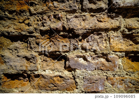 Close-up outdoor view of part of an ancient stone wall with a textured surface. An abstract image of a brown cemented, durable facade. Close-up outdoor view of part of an ancient stone wall with a textured surface. An abstract image of a brown cemented, durable facade. 109096085
