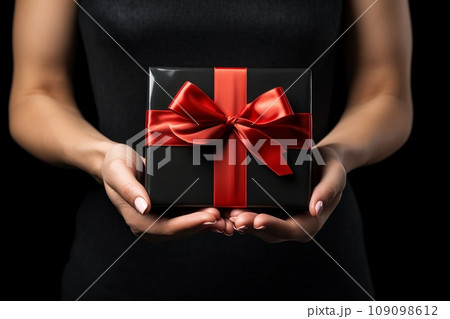 Black Friday sale. Young woman hands holding black gift box with red satin bow on black background. Black Friday sale, promotion, discount, shopping concept. 109098612
