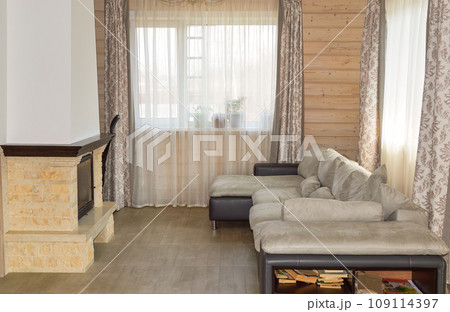 Light living room interior with fireplace, spacious windows, sofa and wooden trim Light living room interior with fireplace, spacious windows, sofa and wooden trim 109114397