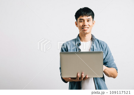 Portrait of a man with a confident smile, typing on a laptop for a successful email or chat session. Studio shot of Asian student isolated on white, showcasing his proficiency in online communication. 109117521