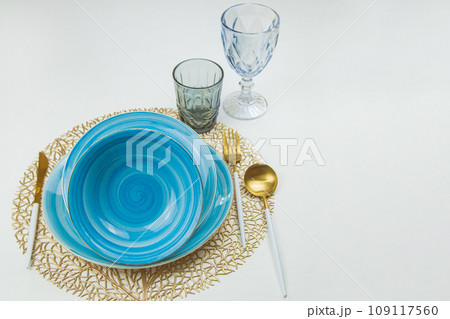 bright blue serving plates with a spiral pattern, one after the other tilted towards the camera, gold - white serving devices are located on the side, behind them are a glass and a cup, side view and 109117560
