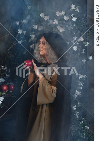 Stepmother witch gives poisoned red apple.Woman as witch in black offers red apple as symbol of temptation, poison. Fairy tale, white snow wizard concept. Spooky Halloween, cosplay. 109119673