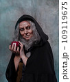 Stepmother witch gives poisoned red apple.Woman as witch in black offers red apple as symbol of temptation, poison. Fairy tale, white snow wizard concept. Spooky Halloween, cosplay. 109119675