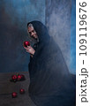 Stepmother witch gives poisoned red apple.Woman as witch in black offers red apple as symbol of temptation, poison. Fairy tale, white snow wizard concept. Spooky Halloween, cosplay. 109119676