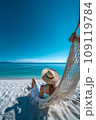Beautiful girl in hat on sandy beach. Woman on seashore relaxing on swing on vacation 109119784