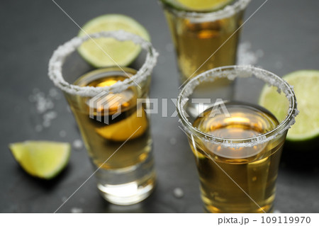 Mexican Tequila shots with salt and lime slices on grey table, closeup 109119970
