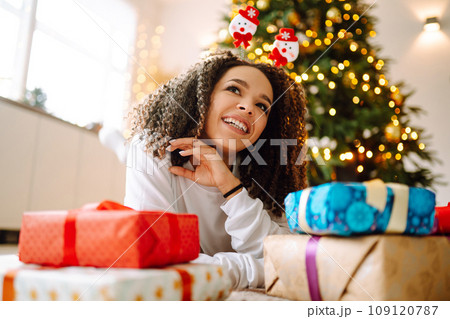 Portrait of young woman in santa claus hat with gift at the Christmas tree. Christmas. New year's. 109120787