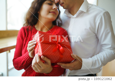 A young man gives his beloved a present and closes her eyes with a hand. Valentine's Day. 109121062