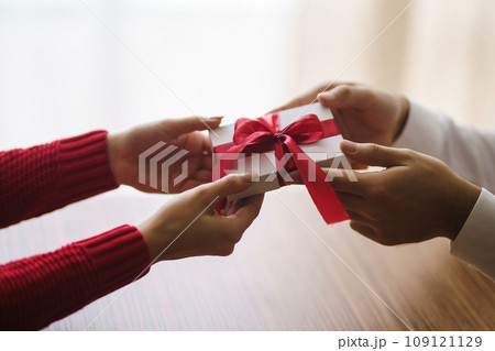 Man gives to his woman a gift box with red ribbon. Hands of man gives surprise gift box for girl. Man gives to his woman a gift box with red ribbon. Hands of man gives surprise gift box for girl. 109121129