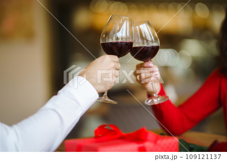 Couple clink glasses with red wine. Lovers give each other gifts. Lovely romantic dinner. 109121137