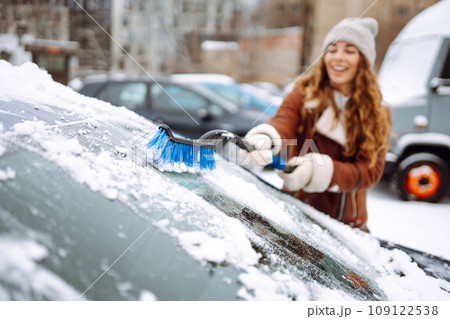 Beautiful woman is cleaning snow from a car with a brush. Transport concept, seasonality 109122538
