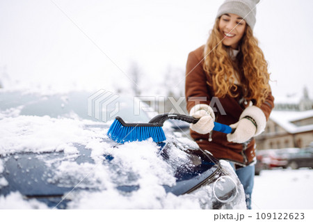 Beautiful woman is cleaning snow from a car with a brush. Transport concept, seasonality Beautiful woman is cleaning snow from a car with a brush. Transport concept, seasonality 109122623